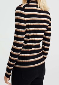 Mujer vistiendo un suéter negro de canalé con rayas horizontales en beige y blanco, combinado con pantalones negros, mostrada de espaldas.