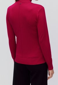 Roter Rollkragenpullover mit langen Ärmeln und taillierter Passform. Verfügt über eine Rückennaht und ein kleines, rundes Knopfdetail am Hals.
