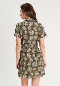 Robe à manches courtes, verte olive, avec un motif floral blanc, taille ceinturée et tissu léger ; présente un col.