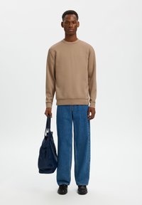 Μπεζ φούτερ με στρογγυλή λαιμόκοψη, ριμπ μανσέτες, συνδυασμένο με άνετο μπλε τζιν παντελόνι. Κρατά τσάντα σε σκούρο μπλε χρώμα, μαύρα παπούτσια ολοκληρώνουν την εμφάνιση.