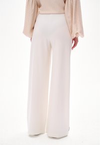Wijdere broek in zacht witte stof, met een hoge taille en een gladde textuur. Naadloos ontwerp met minimale hardwaredetails.