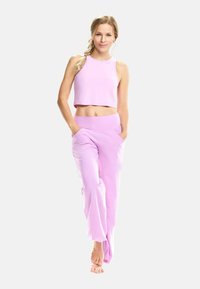 Svijetloružasti crop top i odgovarajuće hlače širokog kroja, s glatkom teksturom i širokim pojasom, bočnim džepovima i opuštenim siluetom.