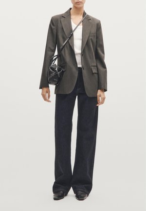 Grijze blazer met een getailleerde pasvorm, gecombineerd met een witte top en donkere denim wijde broek. Inclusief zwarte textuur handtas en scherpe zwarte schoenen.