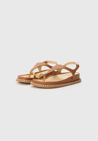 Sandales en cuir marron avec un design à lanière, présentant un anneau d'accent doré et une semelle épaisse avec une couture blanche le long du bord.