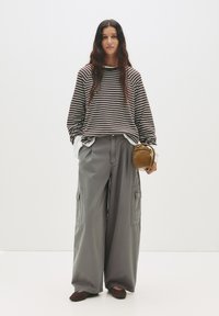 Camicia a maniche lunghe a righe marrone e bianca, abbinata a pantaloni cargo grigi larghi con tasche laterali. Una borsa marrone e scarpe scure completano il look.