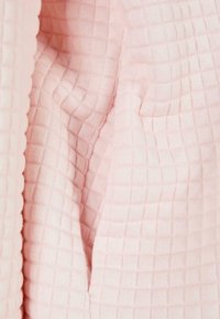 Gros plan d'un tissu rose doux avec un motif de grille en relief et des plis visibles créant texture et profondeur.