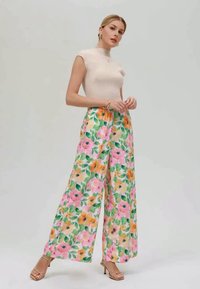 Pantalones anchos con estampado floral en rosa, amarillo y verde; tejido ligero con un estampado vibrante. Combinados con una blusa ajustada color crema y tacones con tiras.