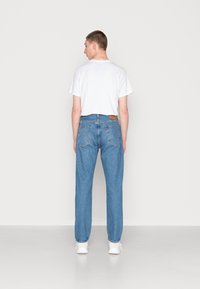 Jenas de ganga azul clara com um corte reto, dois bolsos traseiros e um retângulo de couro castanho na cintura. Combinados com uma t-shirt branca.