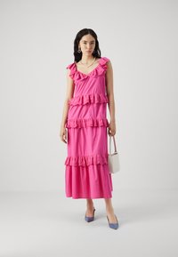 Rochie maxi roz cu volane, bretele reglabile și un corset ajustat. Purtați cu pantofi ascuțiți de un albastru deschis și o geantă mică de culoare crem.