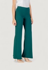 Pantaloni ampi a vita alta di colore teal realizzati in un tessuto morbido, abbinati a tacchi alti color nude, che mostrano una vestibilità sartoriale e linee pulite.