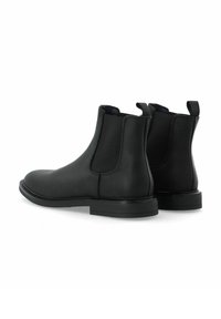 Botas Chelsea de cuero negro con paneles laterales elásticos, punta redondeada y tacón bajo apilado. Textura suave con acentos negros contrastantes.