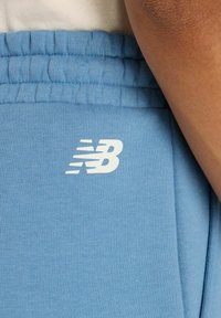 Light blue jogger pants made of soft fabric, featuring an elastic waistband and a white New Balance logo on the left thigh.