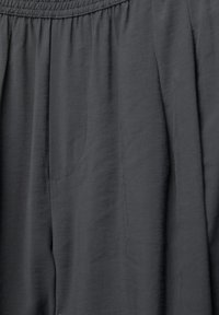 Close-up of dark gray fabric pants with elastic waistband and visible stitching detail on the pocket area.
