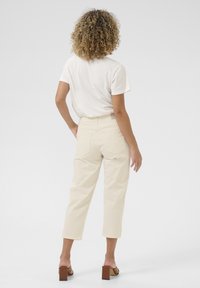 Beige cropped Hosen mit hoher Taille, geraden Beinen und Gesäßtaschen, kombiniert mit einem weißen T-Shirt mit kurzen Ärmeln und braunen Blockabsatzsandalen.