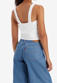 Haut court blanc à fines bretelles associé à un jean en denim bleu taille haute avec une étiquette Levi's et des poches arrière visibles.