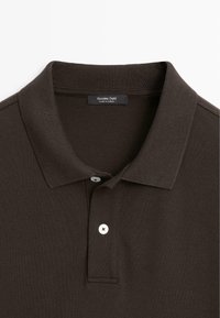 Donkerbruin poloshirt met geribbelde kraag, twee witte knopen en een label "Massimo Dutti Made in Turkey" aan de binnenkant van de hals.