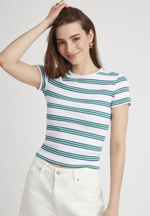 T-shirt ajusté blanc avec des rayures horizontales bleues et vertes, à manches courtes et texture côtelée, associé à un jean blanc taille haute.