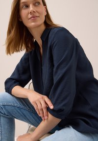 Chemise légère bleu marine au fit décontracté, avec col et manches trois-quarts. Tissu texturé et poignets de manches roulés.