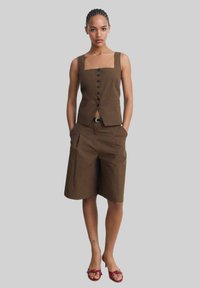 Brown vest top with square neckline and buttons, paired with knee-length brown shorts featuring front pockets. Completed with red sandals.