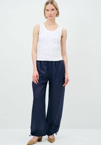 Top bianco senza maniche con decorazioni argentate, abbinato a pantaloni a gamba larga blu navy. L'outfit ha una vestibilità comoda e una trama morbida.