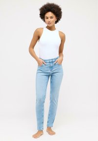 Světlé modré vysoce usazení džíny se slim fit, s předními kapsami a zapínáním na knoflík, kombinované s vypasovaným bílým bezrukávovým body.