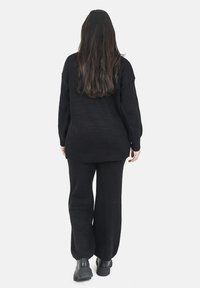 Maglione nero a maglia con maniche a coste, abbinato a pantaloni a gamba larga coordinati. L'outfit presenta una vestibilità comoda e una texture morbida, completato da stivali neri chunky.