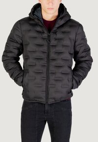 Giubbotto imbottito nero con cappuccio, chiusura con zip e finitura testurizzata caratterizzata da un design a quadri rettangolari. Abbinato a jeans scuri.