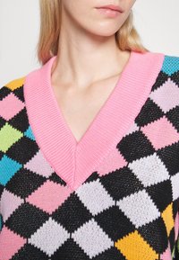 Gebreide pullover met een roze V-hals, zwarte basis en een diamanten patroon in pastelkleuren, met textuuraccenten overal.