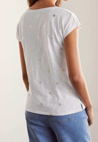 Vit kortärmad topp med mjuk textur, prydd med spridda guldskaldjursmotiv och sidoflikar. Avslappnad design i kombination med denim.