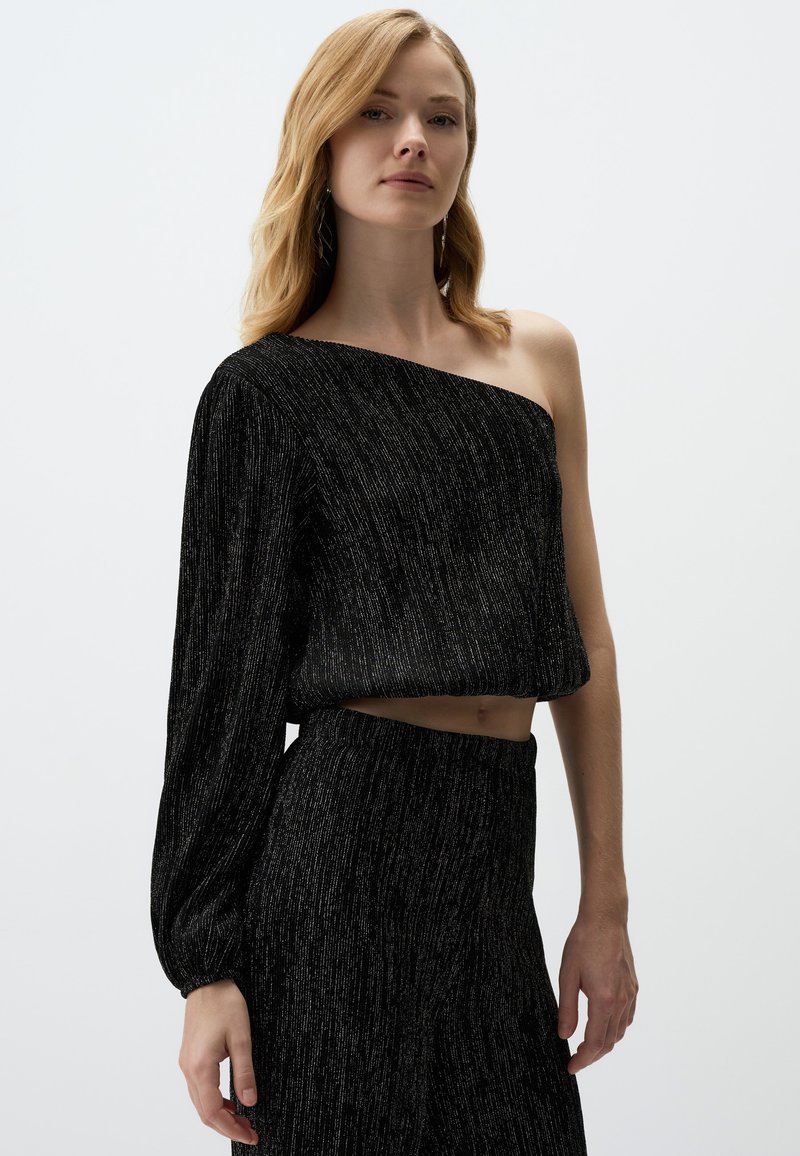 Crop top noir avec une manche longue, tissu texturé, featuring fils métalliques et une coupe ample. Associé à une jupe noire assortie.