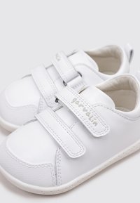 Baskets blanches avec des bandes Velcro, dessus en cuir synthétique lisse, accents texturés, bout rond et semelles intérieures rembourrées pour le confort.