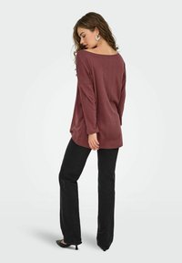 Maglia a maniche lunghe color bordeaux con motivo testurizzato, scollo a barca e vestibilità comoda, abbinata a pantaloni neri a zampa d'elefante e tacchi.