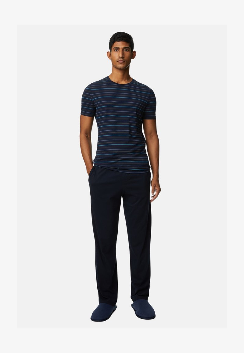 Marine gestreepte T-shirt met korte mouwen, gecombineerd met losse donkere broeken en marine slippers, wat een ontspannen, casual stijl presenteert.