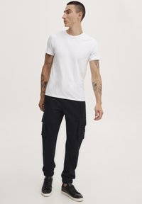 Witte crew neck t-shirt gecombineerd met marineblauwe cargobroek met cargozakken en elastische manchetten; afgewerkt met zwarte sneakers.