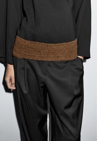Top nero oversize con una cintura intrecciata in tessuto marrone e pantaloni neri, caratterizzati da un tessuto morbido e una silhouette a gamba larga.