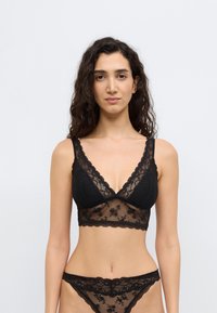 Black lace bralette with V-neck and scalloped edges, featuring floral patterns and sheer detailing, paired with matching lace panties.