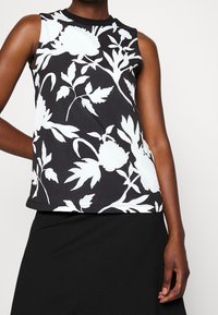 Top sin mangas con estampado floral que presenta un fondo negro con patrones de flores y hojas blancas, confeccionado en una suave tela con un escote redondo.
