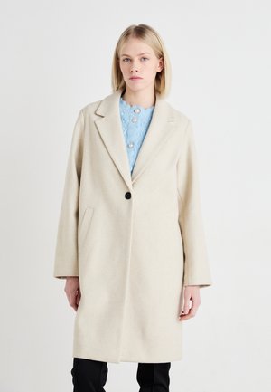 Manteau en mélange de laine beige avec un col cranté, un bouton noir unique, des poches latérales et une silhouette droite, superposé à un haut bleu clair.