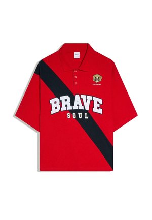 Polo rouge avec une bande diagonale noire, le texte blanc en gras "BRAVE" et plus petit "SOUL", et un blason jaune avec "1990 Champions" sur la poitrine.
