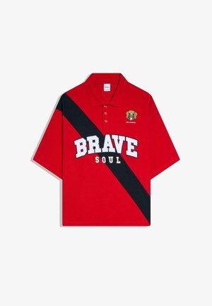 Polo rouge avec une bande diagonale noire, le texte blanc en gras "BRAVE" et plus petit "SOUL", et un blason jaune avec "1990 Champions" sur la poitrine.