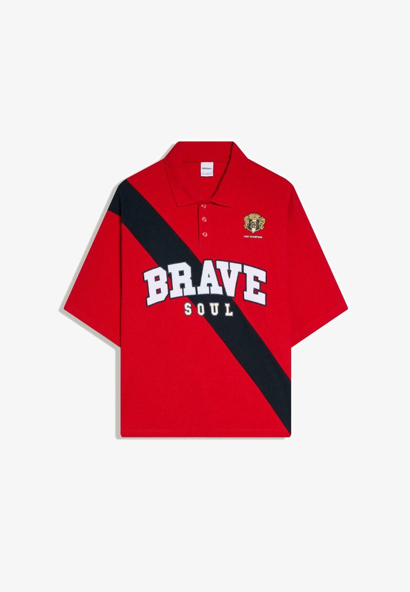 Polo rouge avec une bande diagonale noire, le texte blanc en gras "BRAVE" et plus petit "SOUL", et un blason jaune avec "1990 Champions" sur la poitrine.