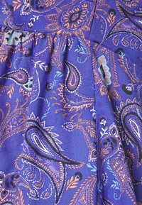 Tecido roxo com um padrão paisley, destacado com detalhes em preto, laranja e azul claro. A textura é suave e tecido, com pregas visíveis.