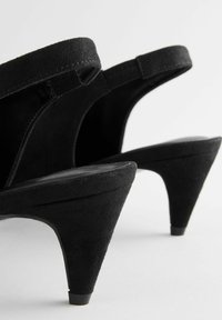 Sandalias de tacón alto de ante negro con parte trasera abierta y tacón afilado. Presenta correas texturizadas y una suela interior suave.