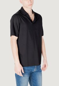 Polo shirt nero a maniche corte con scollatura a V, realizzato in tessuto liscio, abbinato a jeans azzurri chiari. Aspetto semplice e minimalista.