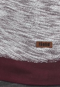 Maglione con un motivo a trama grigia, caratterizzato da un bordo a costine bordeaux e un rettangolo marrone con il nome del marchio "!Solid."