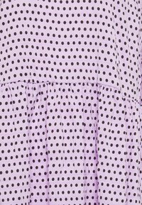 Tecido roxo com bolinhas pretas, apresentando um design em camadas e uma superfície texturizada. O padrão é consistente por todo o material.