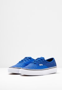 Sneakers in tela blu glitterata con design a bassa altezza, suola in gomma bianca e rifiniture nere. Caratterizzate da punta arrotondata e chiusura con lacci.