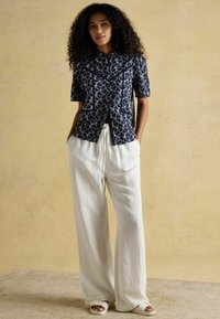 Tumesinise lühikese varrukaga särk, millel on lilleline muster, koos kõrge vöökohtade ja laia jalgadega valgete pükstega ning heledate sandaalidega. Siledad tekstuurid on selgelt nähtavad.