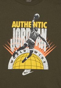 Παίκτης μπάσκετ με το νούμερο 23 πηδά με την μπάλα πάνω από μια κίτρινη σφαίρα, με τα κείμενα «Authentic Jordan» και «World Wide» στο φόντο.