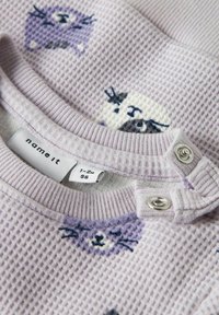 Camiseta morada para bebé con textura de gofre y estampados de animales. Presenta un cuello redondo con broches y etiqueta "name it". Talla 1-2 meses.